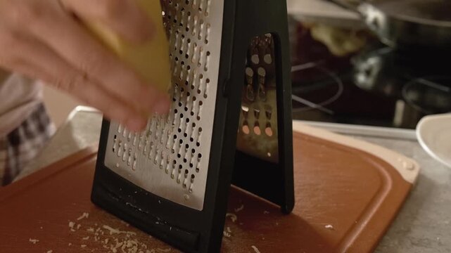 chef grating cheese on box grater for daily meal preparation. cooking with fresh cheese adds great flavor to every hot dish. grated cheese is essential ingredient for tasty hot food