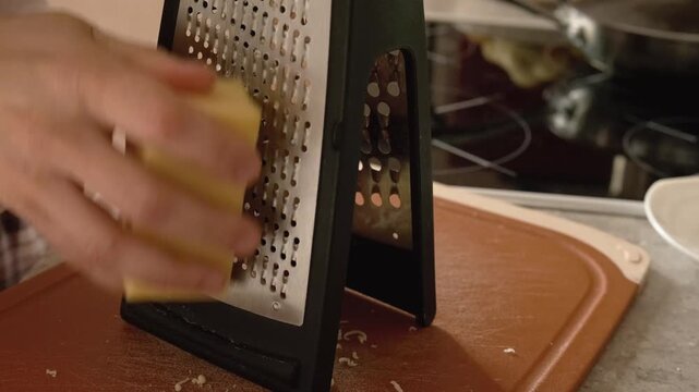 female hand grating cheese on metal grater in kitchen. cooking with fresh cheese for pasta or pizza recipe. preparing cheese is important step for tasty hot meal preparation process