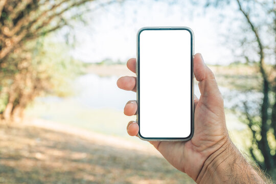 Hand holding a smartphone with blank white screen as mockup copy space outdoors near a river