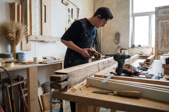 Professional craftsperson restoring window frame in workshop, using hand plane tool at workbench, man carpenter looking checking board surface after smoothing with instrument, master works with plane.