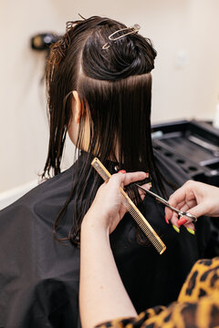 Hairdresser trimming split ends of wet brown hair using scissors and comb with sectioning clips during haircut.