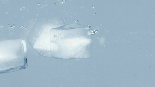 Ice cubes falling into clear water with bubbles and ripples dynamic motion.