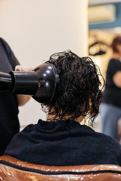 Hairdresser drying wet dark curly hair with diffuser nozzle on hairdryer to form natural curls in beauty salon.