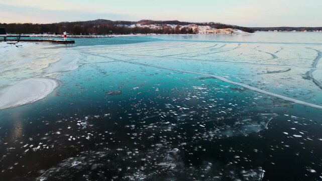 Drone footage captures winter lake with floating ice chunks near shore and lighthouse.