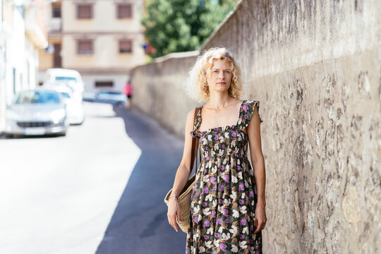 Confident Blonde Woman Standing by Stone Wall on Sunny Residential Street in Spain