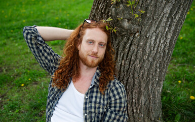 portrait of mature smiling man with red hair stands near a tree and enjoys fresh air in the garden on a summer day. concept without stress. mental health.  Enjoying the little things. World Mental Hea © ulza