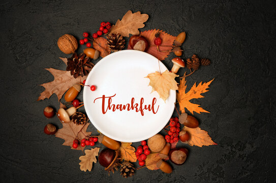 Thanksgiving table setting with fall nature decorations and plate featuring the word "thankful", dark background. symbol of autumn gratitude and celebration, harvest. flat lay