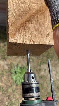 Close up of drilling hole in wooden beam with drill from below outdoors.