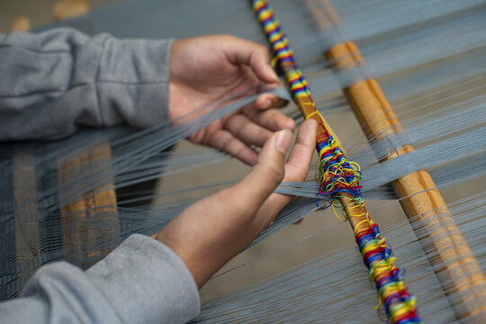 View of hands weaving a traditional Ahuiran reboso on a wooden loom with colorful threads in Ahuiran, Michoacan, Mexico.