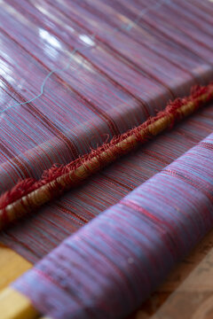 View of the intricate weaving process of a traditional Ahuiran rebozo, showcasing vibrant red and blue threads on a backstrap loom in Ahuiran, Michoacan, Mexico.
