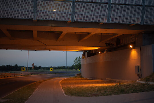 Urban concrete overpass above road and sidewalk, artificial light