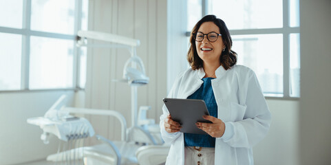 Naklejka premium Dentist using tablet and smiling in bright dental clinic