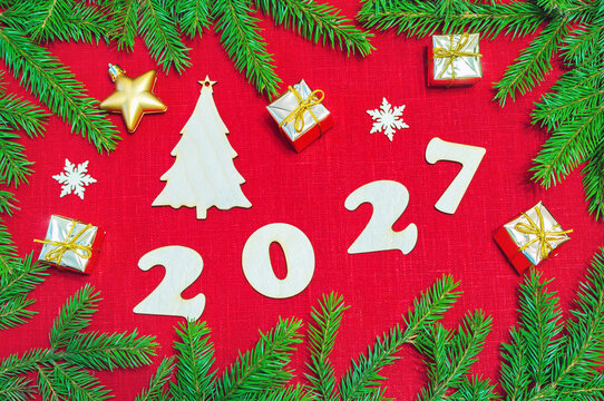 New Year background with 2027 figures, Christmas toys, green fir tree branches making a frame on the red texture linen background. Flat lay, top view