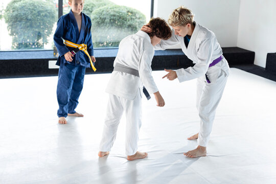 Caring female judo coach supports young student after training exercise while another boy waits nearby. Concept of emotional support, responsible coaching and child wellbeing.