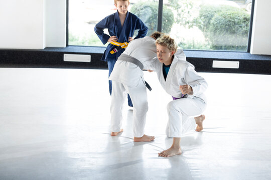 Blonde coach demonstrates low judo stance with child during group lesson. Concept of youth fitness classes, martial arts instruction and sports education.