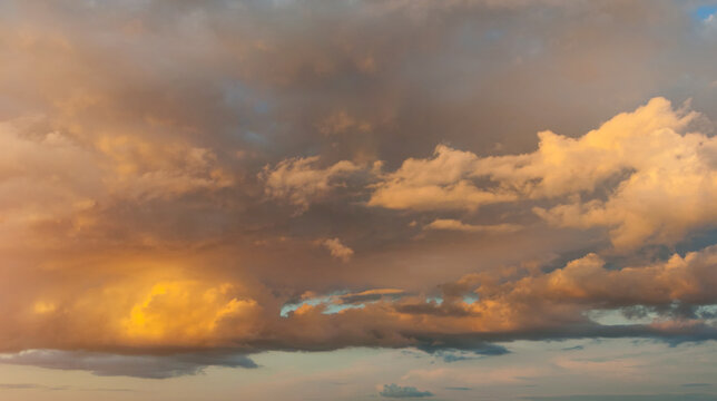 Panoramic wide angle sunset sky background, cloudscape with golden, yellow and orange clouds in the evening sunny sky