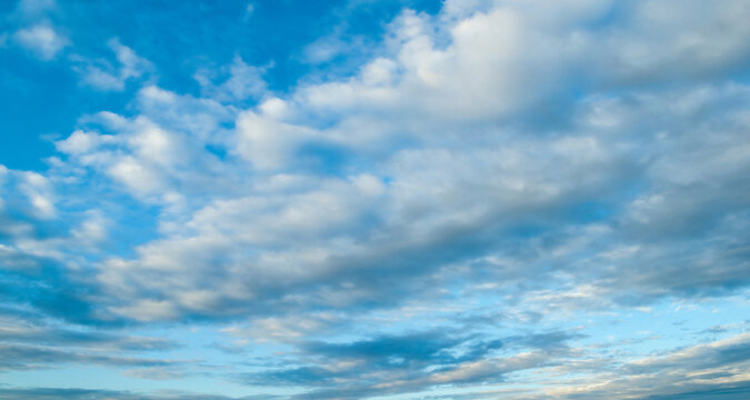 Sweeping blue sky landscape with scenic cumulus clouds at sunset, panoramic background of vast sky in natural colors