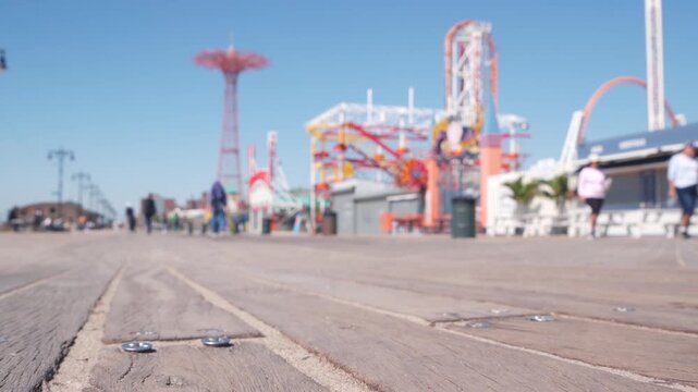 Coney Island beach promenade in Brooklyn, New York, United States. Wooden boardwalk near retro luna park. Amusement park on ocean coast beach. Waterfront summer holiday, people walking on promenade.