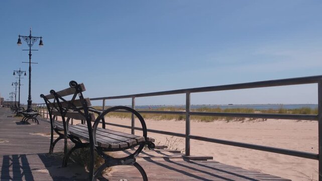 Coney Island beach promenade in Brooklyn, New York, United States. Wooden boardwalk near retro luna park. Benches on ocean coast, sandy beach. Waterfront summer holiday in NYC, USA. Outdoor recreation