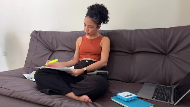 Young latina student studying homework on couch at home