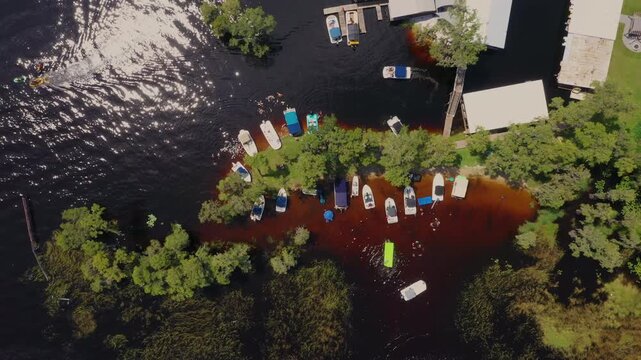 Top-down aerial of boats anchored among cypress trees at Cypress Cove Resort in Clermont, Florida, with wakeboarders and swimmers enjoying the lake.