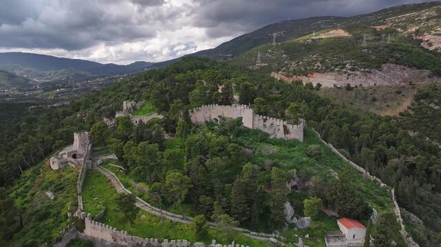 High-altitude drone shot pulling back to reveal the impressive Venetian castle walls of Nafpaktos built on a pine covered hill under a cloudy sky in Lepanto, Aetolia-Acarnania, Greece.