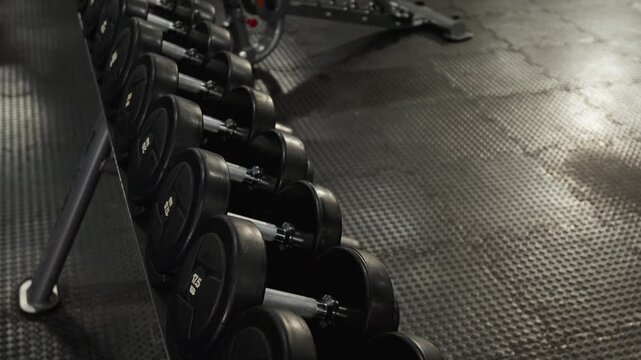 Dumbbells resting on rack in professional gym, camera slowly panning from high angle. Footage ideal for fitness center advertisements, workout motivation content, or sports equipment marketing