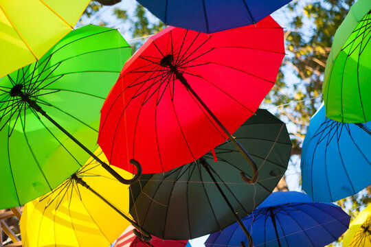 Red, green, yellow, blue, and black umbrellas create a lively canopy outdoors, colorful festival decoration, creative background.