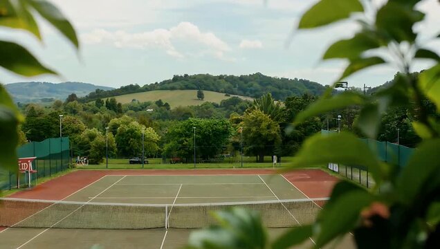 softly defocused high-resolution 4K rural tennis court scene on a cloudy day features blurred green foliage and distant hills creating a calm and moody background perfect for atmospheric