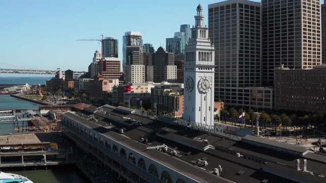 Drone Aerial Beside Historic Ferry Building Clock Tower with Bay Bridge Stretching Across Waterfront - (UHD 4K)