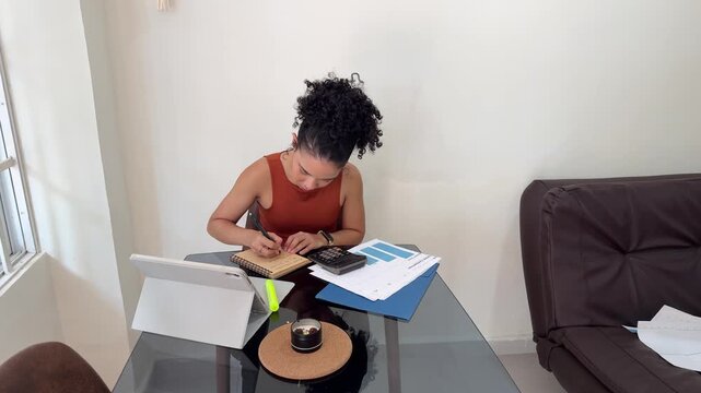 Businesswoman using calculator and writing notes at home office