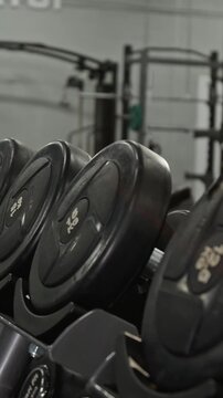 Vertical video of heavy black dumbbells resting on rack in modern fitness center. Footage is perfect for marketing gym memberships, weight training equipment, and athletic lifestyle brands