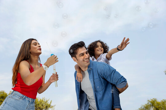 Happy parent with their son having fun with flying bubbles in the park