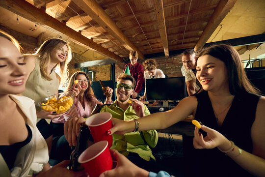 Office friends sharing snacks and colorful drinks during lively company party. Concept of event catering services, beverage delivery pages and employee gathering ads.