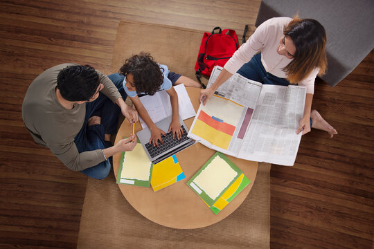 Top view of family members sitting with laptop and newspaper in living room