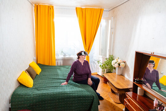 Senior Caucasian woman relaxes with virtual reality glasses after a busy day at home. Comfortable lifestyle and digital entertainment for retirees. Wide shot
