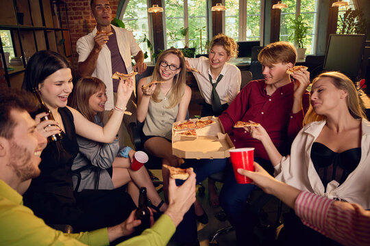 Happy colleagues serving pizza slices during informal office party. Concept of corporate catering services, office lunch delivery and staff event pages.