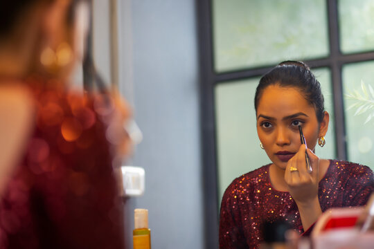 Young woman applying eyeliner in front of mirror
