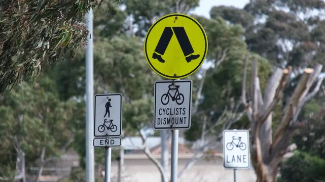 Multiple Australian road traffic signs, including a pedestrian crossing symbol, a "Cyclists Dismount" notice, and shared path markers set against eucalypt trees in Melbourne, Victoria,&nbsp;Australia