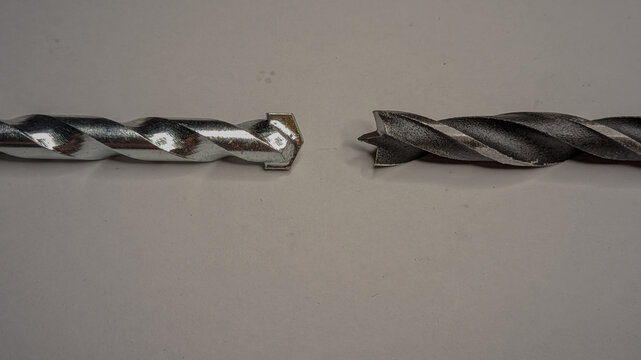 Two different drill bits side-by-side on a plain white surface, a wood brad point drill bit on the left and a carbide-tipped masonry drill bit on the right