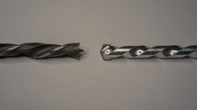 Two different drill bits side-by-side on a plain white surface, a wood brad point drill bit on the left and a carbide-tipped masonry drill bit on the right