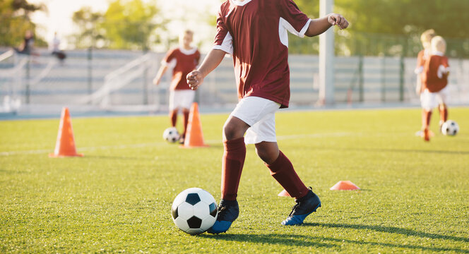 Junior Soccer Player Dribbling Ball Through Orange Agility Cones - Youth Football Training Practice Session on Green Turf Field