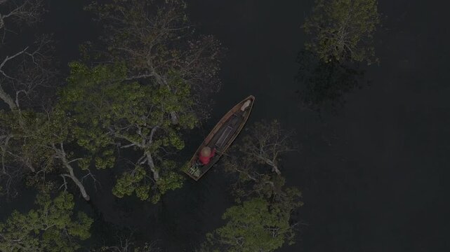 Aerial drone view of a fisherman rowing across Tuyen Lam Lake at sunrise near Suoi Tia in Xuan Huong, Da Lat, Vietnam, surrounded by peaceful pine forests.