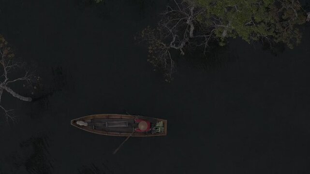 Aerial drone view of a fisherman rowing across Tuyen Lam Lake at sunrise near Suoi Tia in Xuan Huong, Da Lat, Vietnam, surrounded by peaceful pine forests.