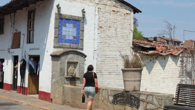 Woman approaching Pila del Tecolote owl fountain on a traditional street in Tapalpa Pueblo M&aacute;gico, Jalisco, Mexico. Tourist visiting local cultural landmark.