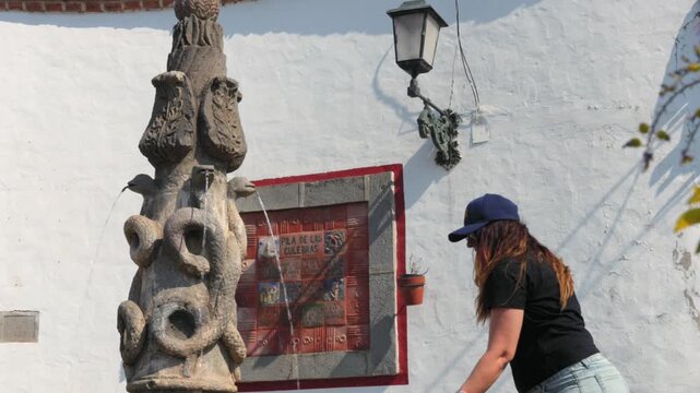 Woman tourist touching flowing water at Pila de las Culebras serpent fountain in Tapalpa Pueblo M&aacute;gico historic center, Jalisco, Mexico. Travel lifestyle shot.