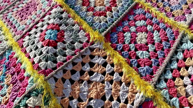 4K close-up video of a colorful handmade crochet granny square with detailed yarn texture and traditional pattern. Creative needlework, textile craft, slow fashion and handmade design.