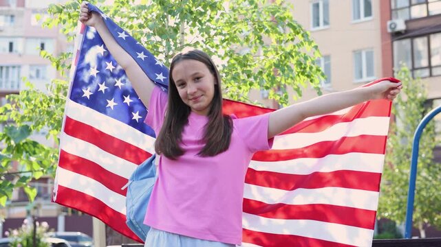 Happy teenage girl with backpack holding an American flag, student exchange program and studying abroad concept