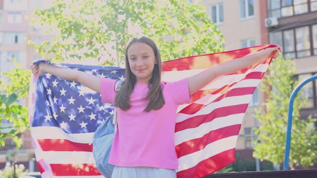 Happy teenage girl with backpack holding an American flag, student exchange program and studying abroad concept