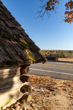 View of a historic log cabin with a mossy wooden shingle roof and autumn foliage beside a road at Valley Forge, Pennsylvania, United States.